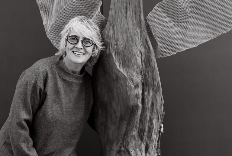 Eliana Carvalho ao lado de uma escultura de madeira com elementos de tela metálica