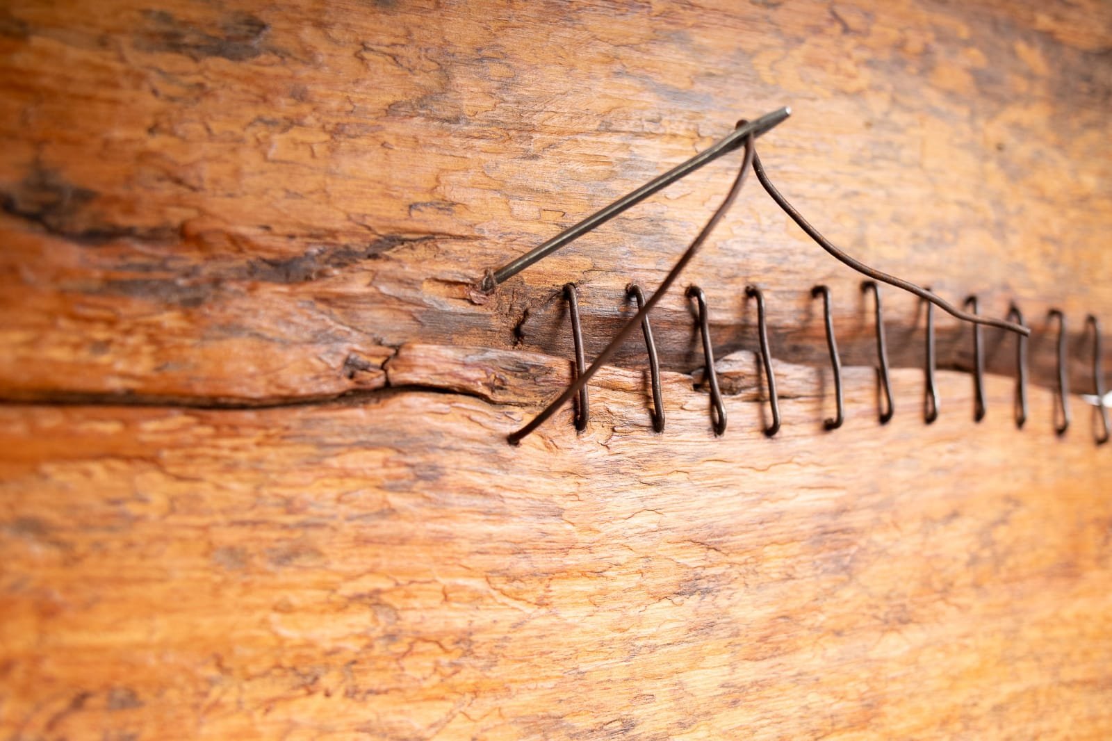 Superfície de madeira com linhas de metal e um alfinete cravado nela como se estivesse sendo costurada